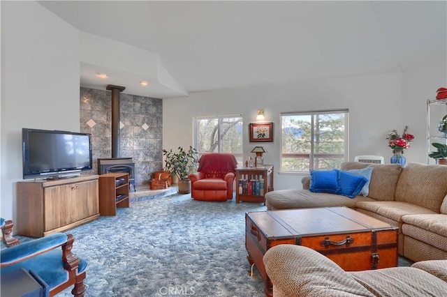 living area with carpet, lofted ceiling, a wood stove, and a healthy amount of sunlight