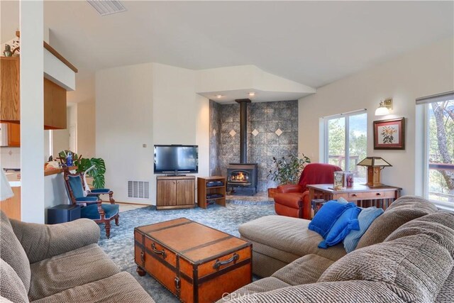 living area featuring lofted ceiling, a wood stove, visible vents, and carpet floors