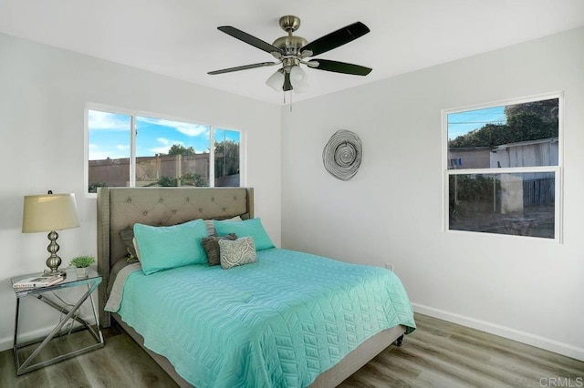 bedroom with multiple windows, a ceiling fan, baseboards, and wood finished floors