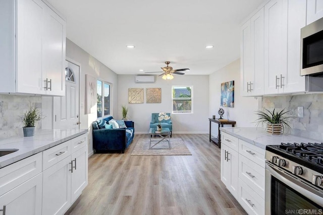 kitchen featuring open floor plan, stainless steel appliances, light wood-style floors, and light stone countertops