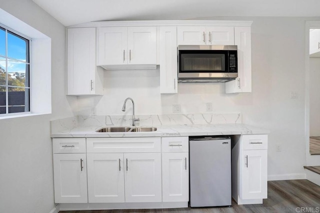 kitchen featuring a sink, stainless steel microwave, light stone counters, and white cabinets