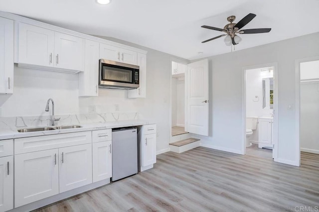 kitchen featuring dishwashing machine, light stone counters, a sink, white cabinets, and stainless steel microwave