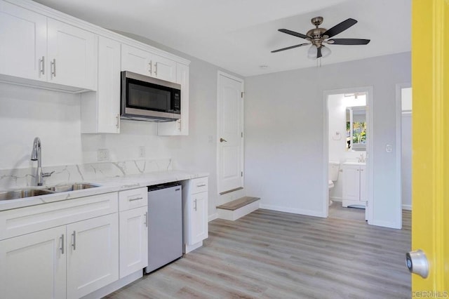 kitchen featuring stainless steel microwave, light stone counters, dishwashing machine, white cabinets, and a sink