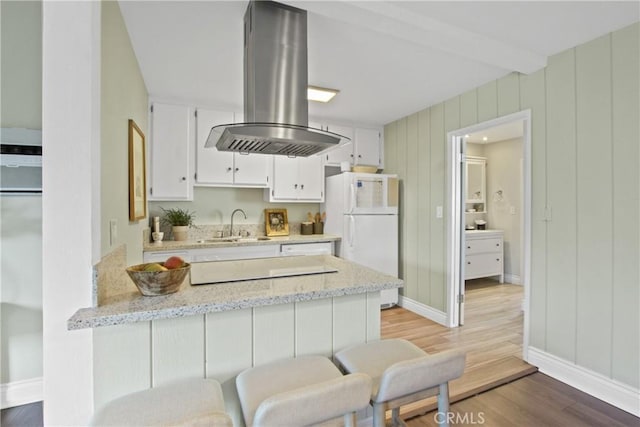 kitchen with a peninsula, freestanding refrigerator, light wood-style floors, white cabinetry, and island range hood