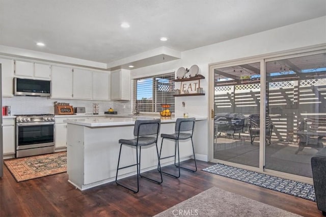 kitchen featuring dark wood-style floors, a peninsula, stainless steel appliances, light countertops, and backsplash