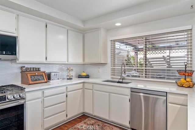 kitchen with light countertops, decorative backsplash, white cabinets, stainless steel appliances, and a sink