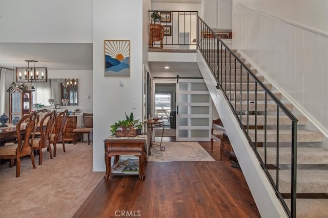 entryway featuring wood finished floors, an inviting chandelier, stairs, a towering ceiling, and a barn door