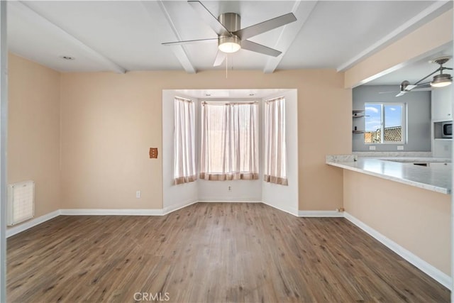 interior space featuring beam ceiling, wood finished floors, baseboards, and ceiling fan