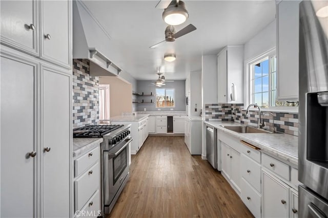 kitchen featuring a sink, stainless steel appliances, light countertops, white cabinets, and wall chimney range hood