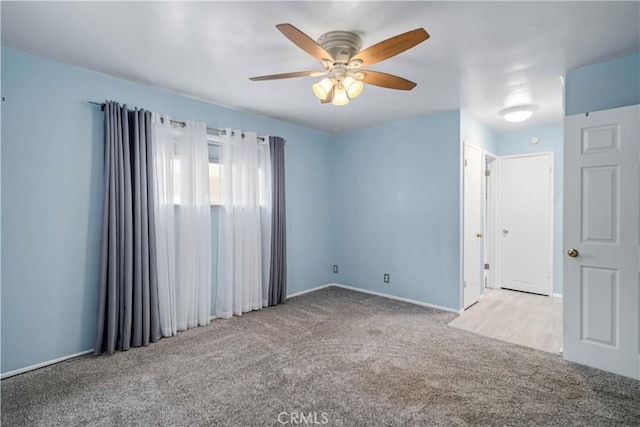 carpeted spare room featuring baseboards and a ceiling fan