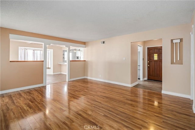 unfurnished living room with visible vents, wood finished floors, baseboards, and a textured ceiling