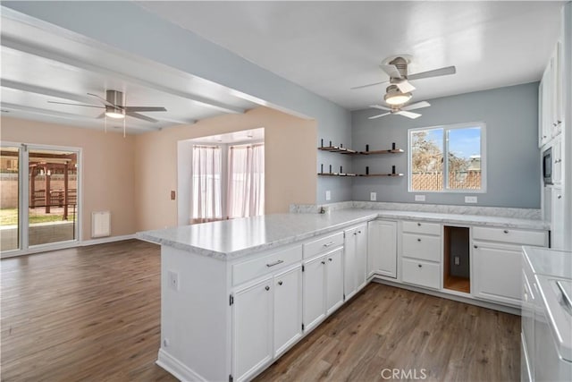 kitchen with wood finished floors, a peninsula, open shelves, white cabinets, and open floor plan