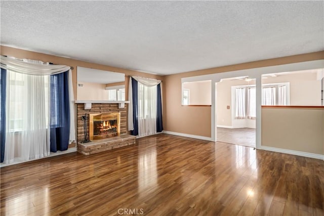 unfurnished living room with a fireplace, a textured ceiling, baseboards, and wood finished floors