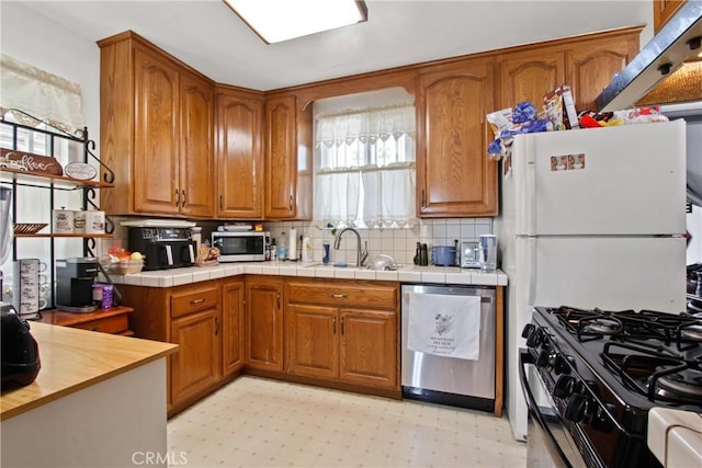 kitchen with a sink, stainless steel appliances, brown cabinetry, decorative backsplash, and light floors