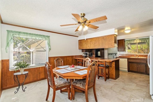 dining room with a textured ceiling, wooden walls, and wainscoting