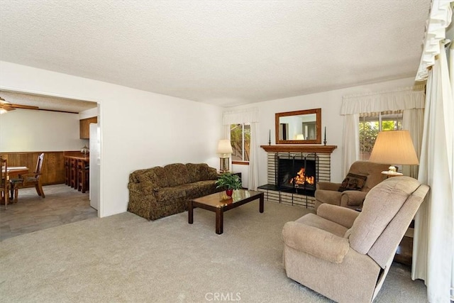 living room with carpet floors, a textured ceiling, a brick fireplace, and a ceiling fan