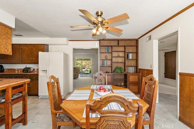 dining space with a textured ceiling, a ceiling fan, visible vents, and wainscoting