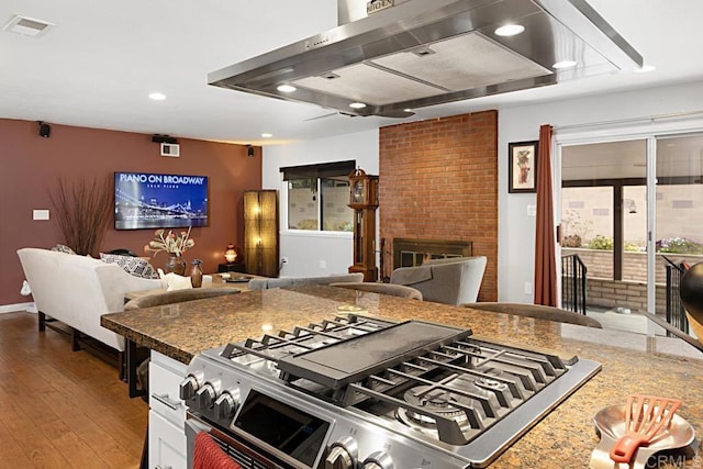 kitchen featuring visible vents, a brick fireplace, open floor plan, range hood, and wood finished floors