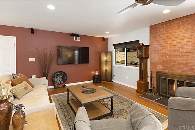 living area with ceiling fan, baseboards, a brick fireplace, and wood finished floors