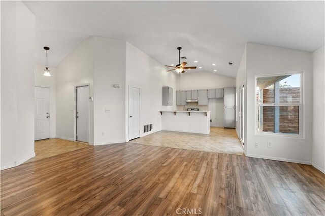 unfurnished living room with high vaulted ceiling, ceiling fan, light wood-type flooring, visible vents, and baseboards