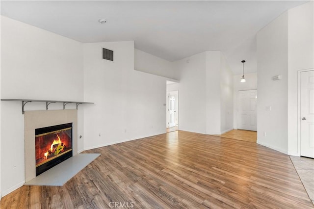 unfurnished living room featuring a glass covered fireplace, wood finished floors, and a high ceiling