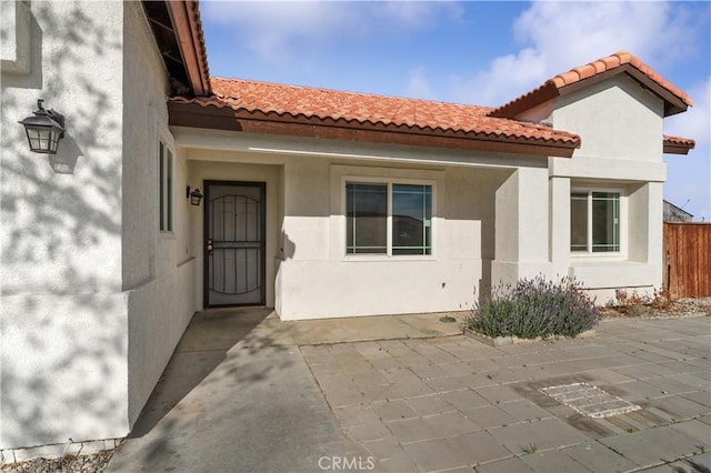 property entrance featuring stucco siding, fence, a patio area, and a tiled roof