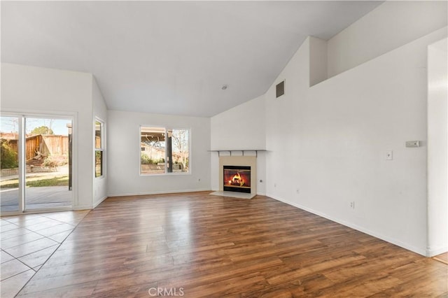 unfurnished living room with a fireplace with flush hearth, wood finished floors, baseboards, and visible vents