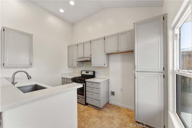 kitchen featuring stainless steel range with gas stovetop, a sink, lofted ceiling, gray cabinets, and under cabinet range hood