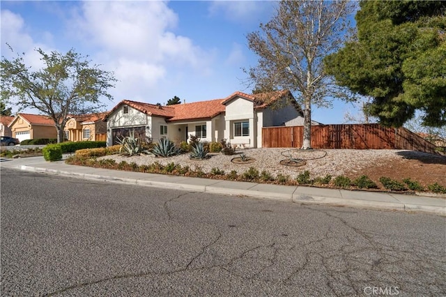 mediterranean / spanish house featuring a garage, stucco siding, fence, and a tile roof