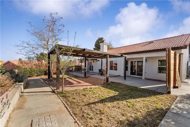 rear view of property featuring a chimney, a patio area, stucco siding, and a tile roof