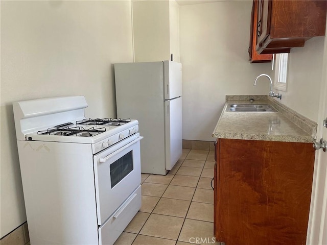 kitchen with light countertops, light tile patterned floors, brown cabinetry, white appliances, and a sink