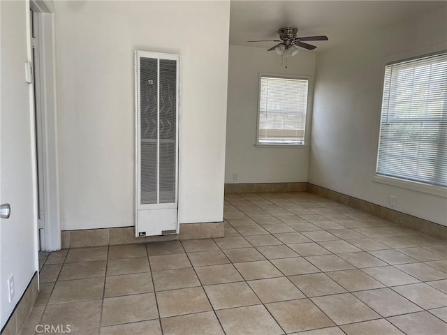 unfurnished room featuring ceiling fan, a wealth of natural light, a heating unit, and light tile patterned floors