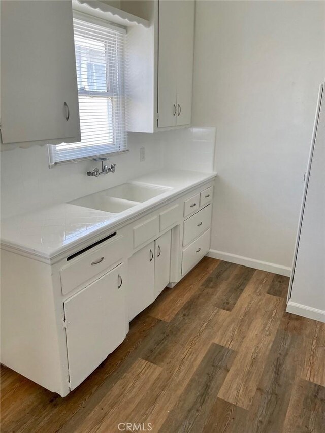 kitchen with a sink, wood finished floors, white cabinets, and light countertops