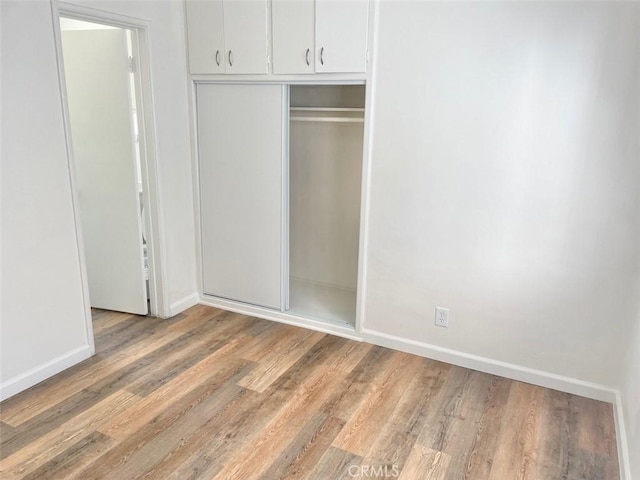 unfurnished bedroom with baseboards, light wood-type flooring, and a closet