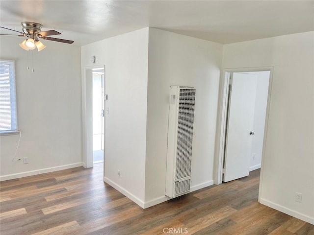 empty room with baseboards, a heating unit, a ceiling fan, and wood finished floors