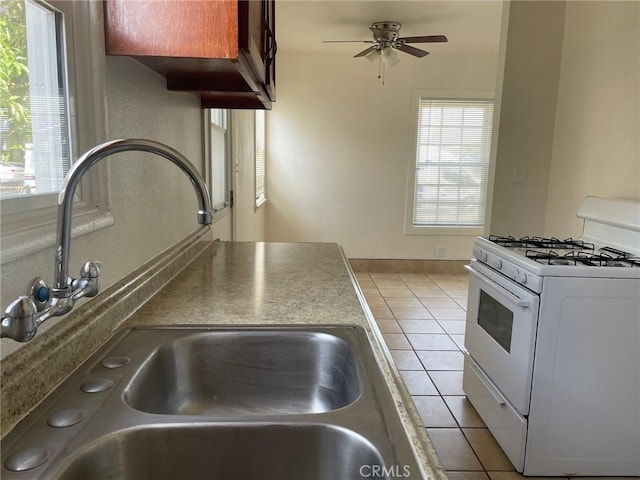 kitchen with a sink, white gas range oven, light tile patterned floors, baseboards, and ceiling fan