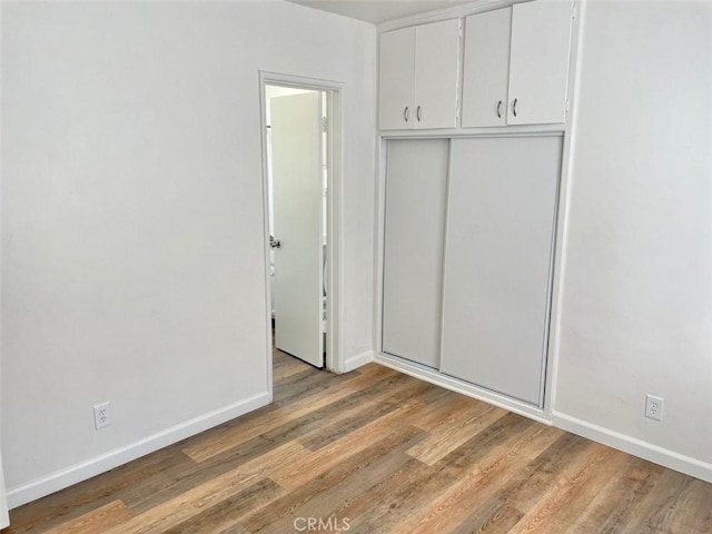 unfurnished bedroom with light wood finished floors, a closet, and baseboards