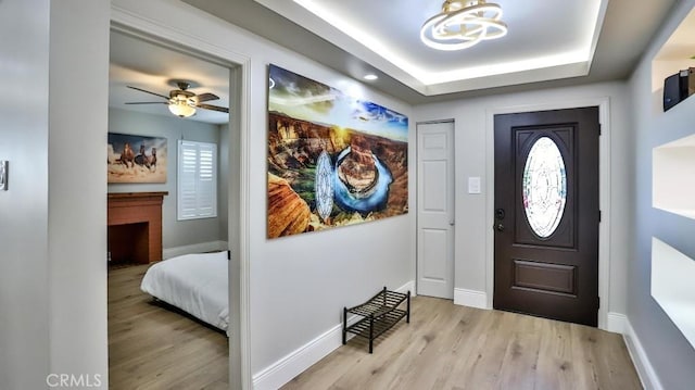 entryway with a fireplace, a raised ceiling, wood finished floors, and baseboards