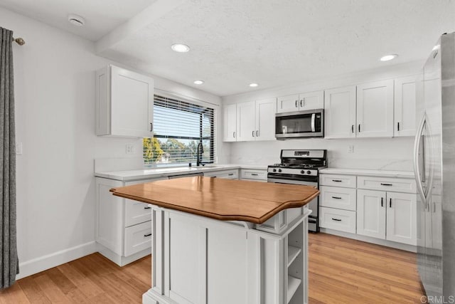 kitchen with butcher block countertops, light wood-style floors, appliances with stainless steel finishes, white cabinetry, and a center island