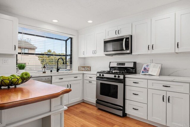 kitchen with light wood finished floors, a sink, recessed lighting, white cabinetry, and appliances with stainless steel finishes