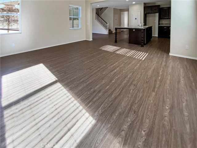 unfurnished living room featuring dark wood-type flooring, stairway, baseboards, and a sink