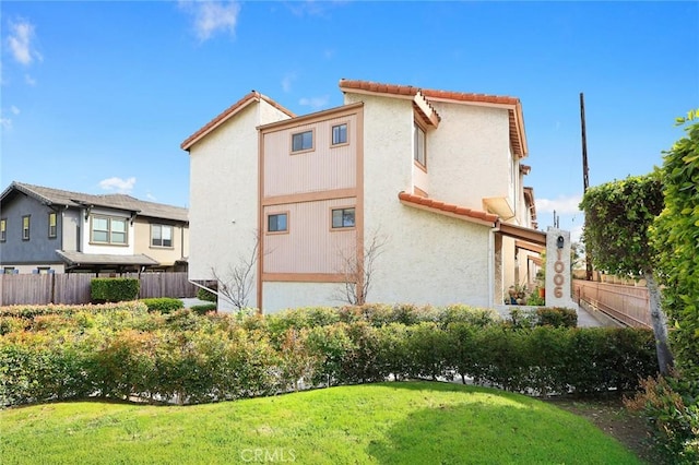 view of home's exterior featuring a tiled roof, a lawn, stucco siding, and fence