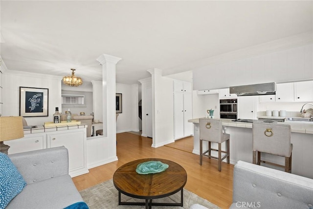 living room featuring a notable chandelier, light wood-style flooring, decorative columns, and ornamental molding