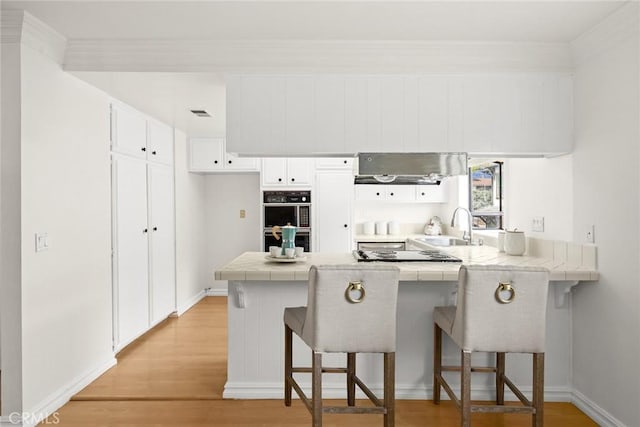 kitchen featuring a peninsula, a sink, tile counters, a kitchen bar, and light wood-type flooring