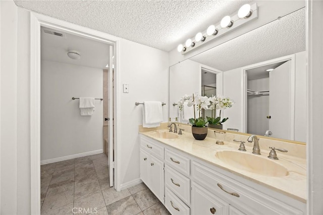 full bathroom with a textured ceiling, double vanity, baseboards, and a sink