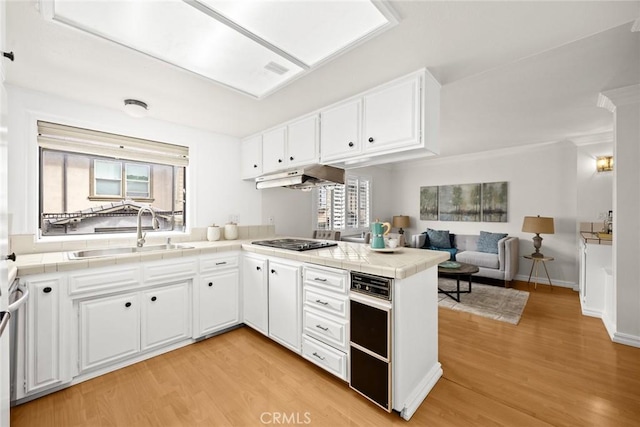 kitchen with tile countertops, a peninsula, gas stovetop, a sink, and under cabinet range hood