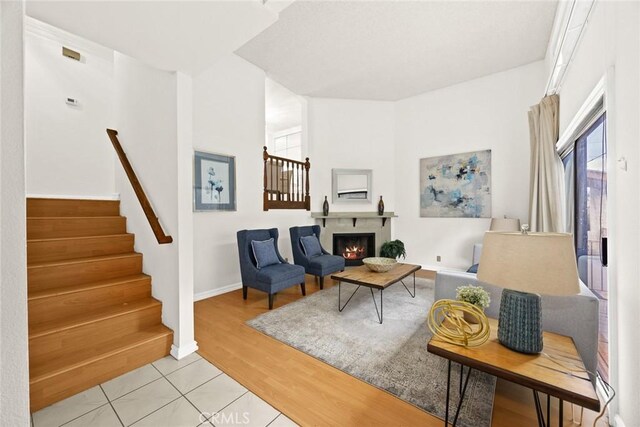 living area with stairs, baseboards, light wood finished floors, and a lit fireplace