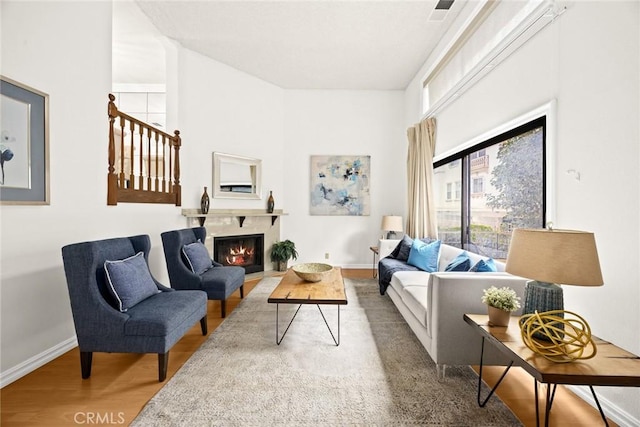 living room with wood finished floors, visible vents, baseboards, a lit fireplace, and stairs