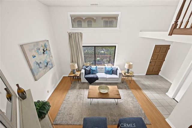 living room with visible vents, baseboards, a towering ceiling, and wood finished floors