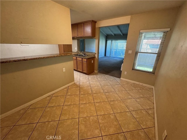 kitchen featuring a sink, baseboards, brown cabinets, and light tile patterned flooring